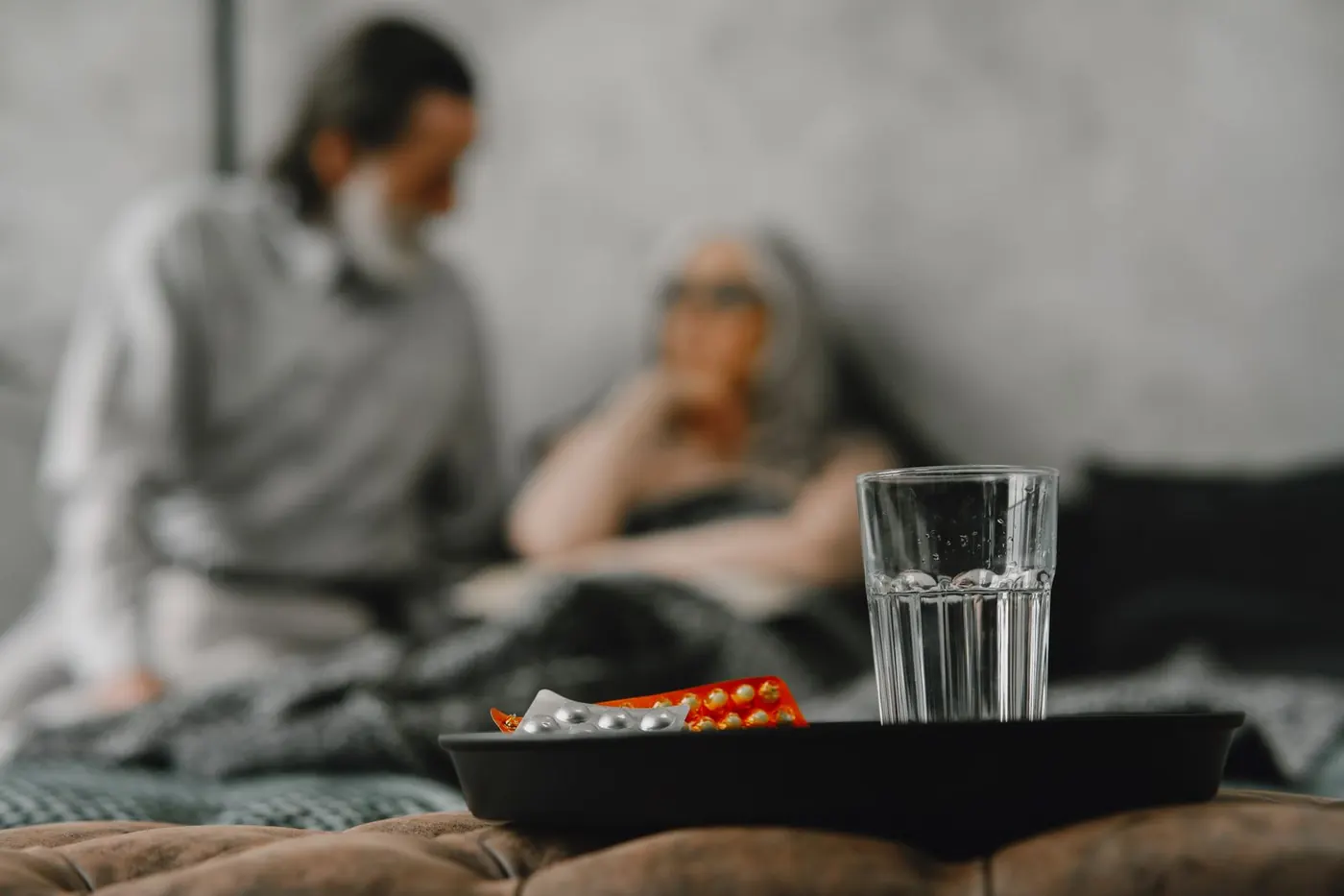 Glass of water and a blister pack on a tray, an older couple in soft focus behind